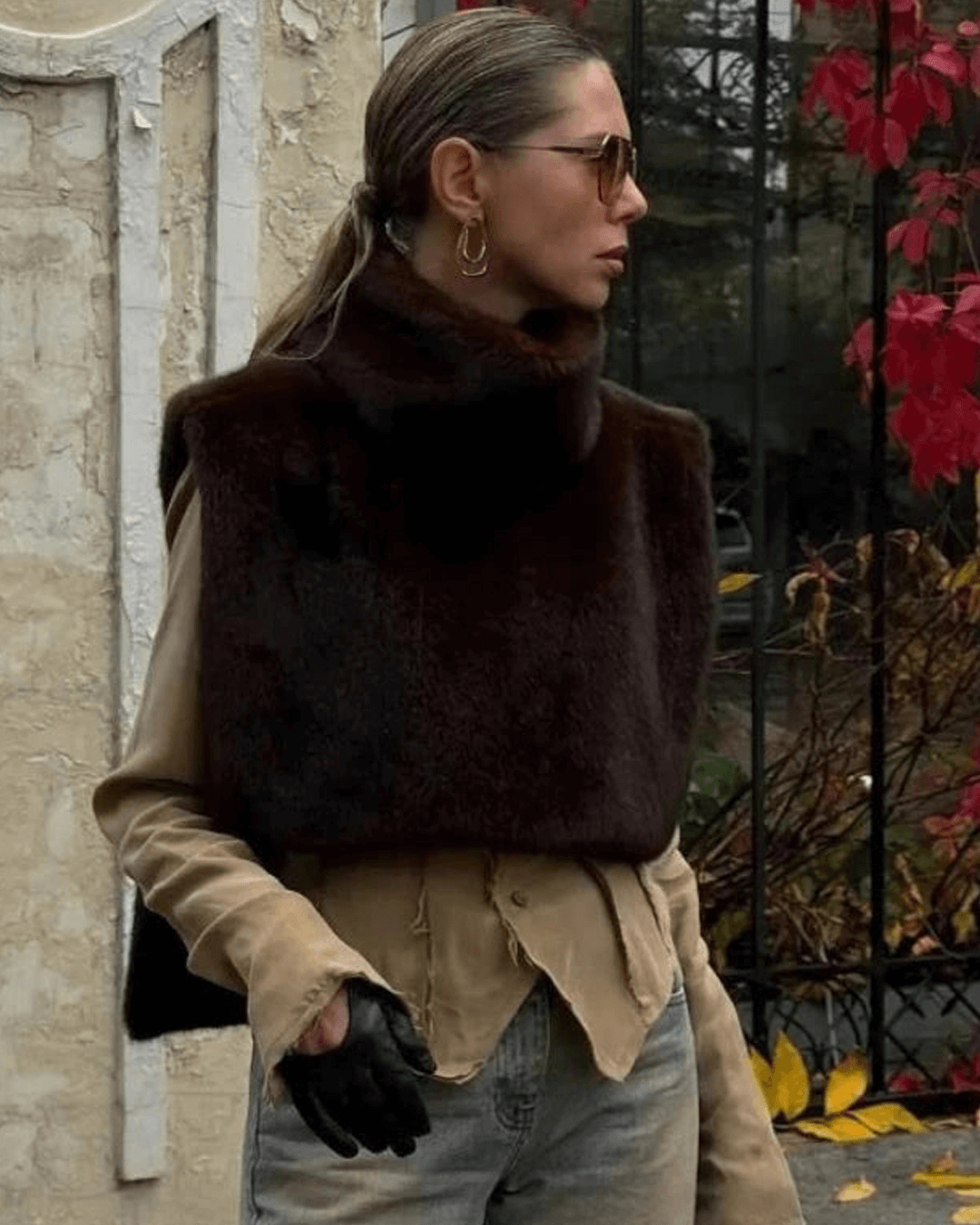 Woman wearing a brown fur vest over a beige shirt with a blurred background
